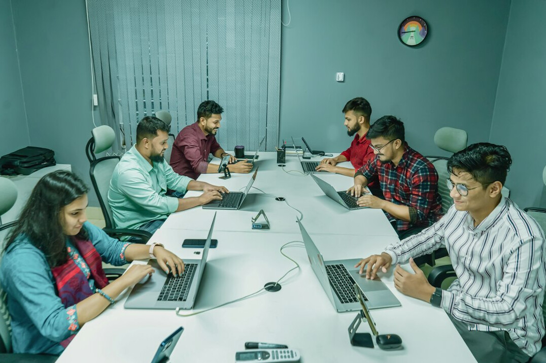 Colleagues working together at a shared desk with laptops
